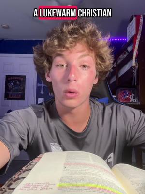 A young man with curly blonde hair looks directly at the camera in a room with a religious cross on the background wall. The image is well-lit, and appears to be taken from a selfie perspective, with the creator's upper body and a book in the foreground. The video includes an overlay text that says "A Lukewarm Christian."