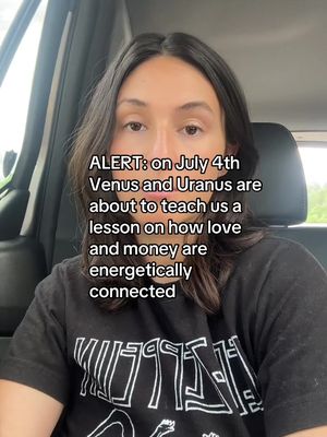A woman in a black t-shirt with white text is centered in the frame. She has dark hair and is looking directly at the camera. Text overlay in white font states: "ALERT: on July 4th Venus and Uranus are about to teach us a lesson on how love and money are energetically connected."