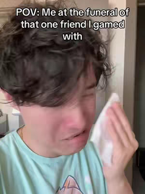 A close-up shot of a young man, appearing to be crying, with a tissue in his hand. He's wearing a light blue t-shirt and a gold chain is visible. The background is a slightly blurred room with a doorway on the right.