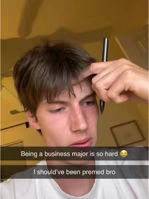 A young man looking down with a contemplative or frustrated expression, holding a pen up to his forehead. Text overlays at the bottom offer context.