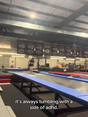 The image shows a young woman in a gymnastics gym, standing on a long trampoline. Behind her, there are several banners and some people are visible in the background. There is a text overlay at the bottom of the image.