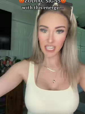 A woman with long blonde hair is speaking directly to the camera with sunglasses perched on her head. The background is a room with white panels, and a television is visible in the background. The woman is wearing a cream-colored tank top and jewelry. Text is overlaid at the top of the screen.
