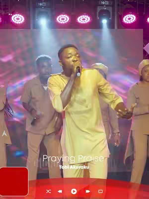 The cover image shows a live performance. A man in a yellow tunic-style shirt stands center stage, holding a microphone and singing. He is surrounded by other performers, and the background features stage lighting and a screen. Text overlayed on the image reads "Praying Praise" and identifies the performer as Tobi Akuraku.