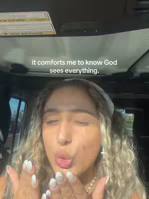 A selfie taken from inside a vehicle. The main subject is a young woman with light skin and long, wavy blonde hair. She is wearing a white headband. She is blowing a kiss towards the camera with her lips pursed. The background is blurred but suggests an outdoor setting, with glimpses of trees and sky visible through the windows. The image utilizes natural lighting, highlighting the woman's features and the interior of the vehicle. Text overlayed on top of her head.