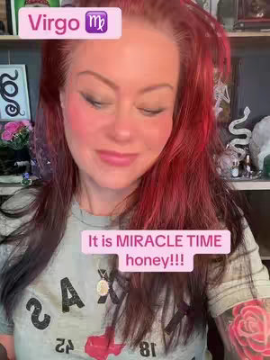 A woman with red hair and a light green t-shirt is looking down with pink cheeks. There is a pink rectangle over her head indicating the zodiac of "Virgo" at the top. Another pink rectangle is floating over the bottom middle of the photo with the text"it is MIRACLE TIME honey!!!".