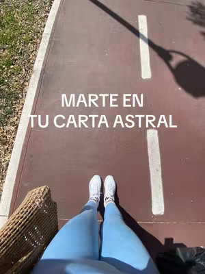 The image shows a top-down shot of a person's legs and feet, standing on a reddish-brown surface with white stripes. The person is wearing light blue leggings and white shoes. The text overlay reads, "MARTE EN TU CARTA ASTRAL."