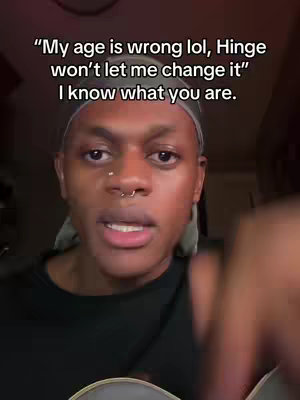 A close-up shot of a person with dark skin, brown eyes, and a septum piercing. The person is looking directly at the camera with a neutral expression. Above them, text overlays read, 'My age is wrong lol, Hinge won't let me change it
I know what you are.'