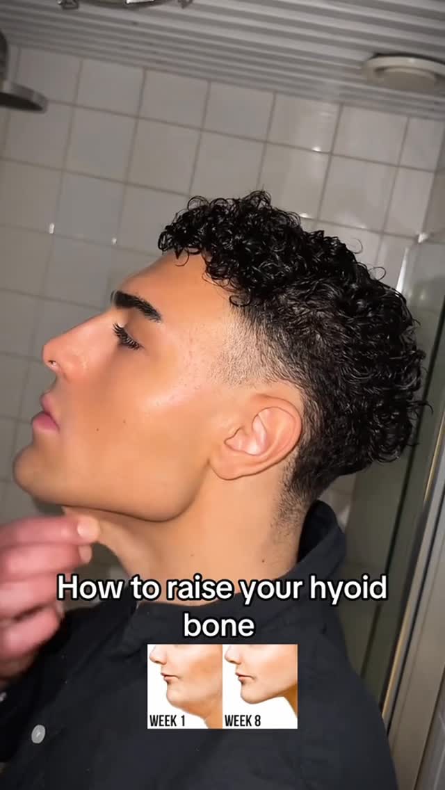A side profile of a man with dark, curly hair and a shaved undercut, appearing to be in a bathroom with white tiled walls. He's looking upwards, with the focus on his jawline and neck as he demonstrates something. Text overlayed reads 'How to raise your hyoid bone' with before-and-after jawline comparison images.