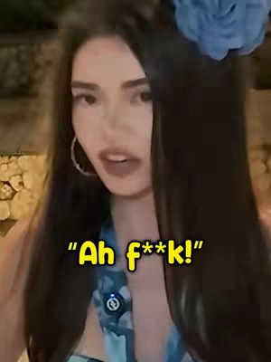 A woman with long dark hair, a blue floral hair accessory, and large hoop earrings is looking at the camera with an expression of surprise or exasperation. A text overlay reads: 'Ah f**k!'