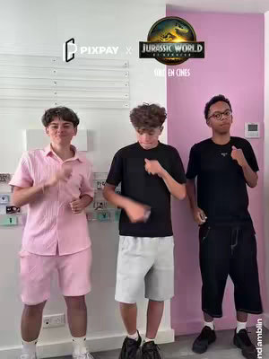 Three young men dancing in a room. The man on the left is wearing a pink outfit, the man in the middle is wearing a black tshirt and white shorts and the man on the right is wearing a black outfit with glasses. Behind them is a pink wall and some decor elements on the left wall. There's a logo of a well-known animated series.