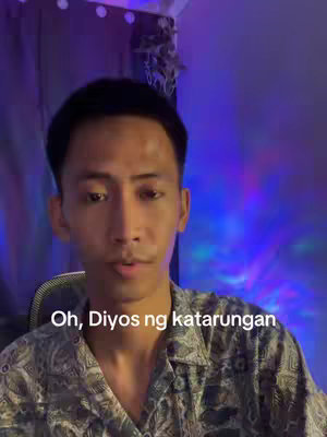 A man with short black hair is looking towards the camera. He is wearing a patterned shirt and is positioned in front of a blurred purple and blue background.