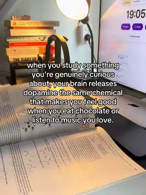 The image shows a desk setup with an open textbook and a pile of books, a book stand, headphones and a lamp with a lit bulb, a timer on the desktop and a phone next to it. The foreground features the open book with text. Overlayed text provides information on what happens in the brain when studying.