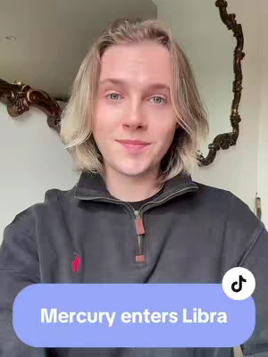A young man with fair skin and blonde, shoulder-length hair is the central figure in a selfie-style shot. He is wearing a dark gray zip-up sweater with a red polo horse logo on the left side. The background appears to be a domestic interior. The video overlay features a light purple rectangular graphic with white text.