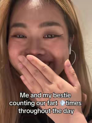 A selfie of a woman with light brown hair, holding her hand over her mouth, laughing. Text overlayed at the bottom of the image: "Me and my bestie counting our fart times throughout the day." The background appears to be a white wall.