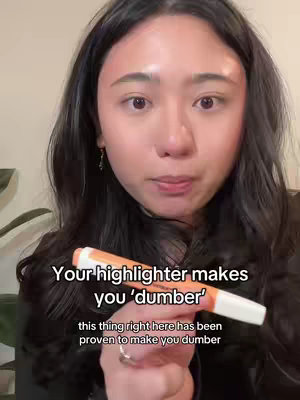 A woman with long dark hair holds an orange highlighter and speaks to the camera. Text overlays read, 'Your highlighter makes you 'dumber'' and 'this thing right here has been proven to make you dumber'.