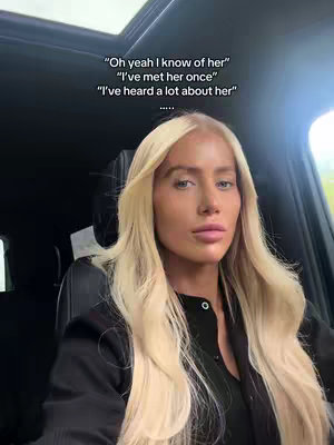 A woman with long blonde hair is seated in a car looking at the camera. Text overlays frame her face, and the interior of the car is visible.