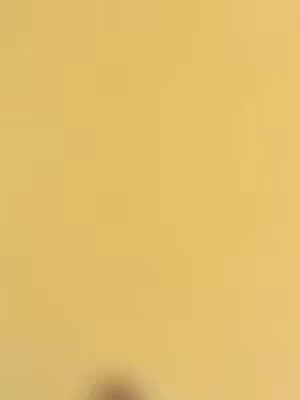 The cover image is a solid, muted yellow background. In the bottom center, a blurred, dark shape suggests a person or object is present, but their features and details are indistinguishable due to the lack of focus.