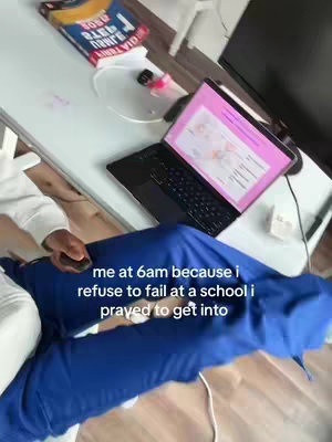 The image shows an overhead shot with the creator, wearing blue scrubs, seated at a desk. On the desk is a laptop displaying what appears to be medical information. Beside the laptop are books. The lighting is bright, suggesting a well-lit environment.