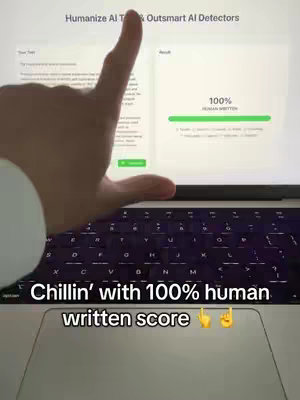 A person's hand points to the screen of a laptop displaying text and a progress bar. Below the laptop is a text overlay: “Chillin’ with 100% human written score” with emojis of a thumbs up.
