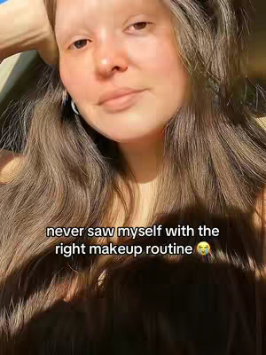 A woman with long brown hair is centered in the frame, slightly angled towards the viewer and looking downwards. The background is blurred, suggesting an outdoor setting. Overlay text stating, 'never saw myself with the right makeup routine', is at the bottom.