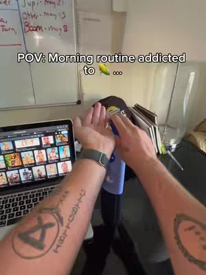 The image shows a first-person perspective of a person's hands holding a blue bottle. A laptop with potentially explicit content is open in the background. The person's arm, covered in tattoos, is also visible.