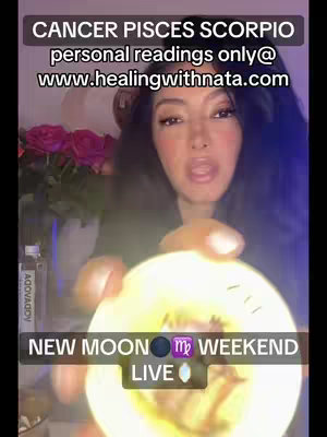 A woman with long dark hair is centered in the frame. The image is lit with a purple and orange color palette. She is holding a glowing orb in her hands, and the background is softly blurred with some pink flowers.