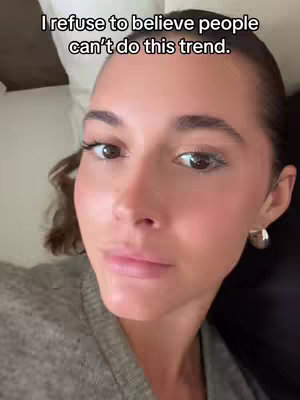 A close-up shot of a woman's face, with a close-up of her face in the center, slightly off-center, showing her eyes, nose, and mouth. The woman has dark hair and is wearing a grey top. Above her head, the text overlay is visible.