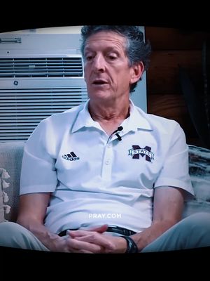A man in a white polo shirt with an Adidas logo and the Mississippi State logo is seated indoors in front of a white air vent. The image is lit by a natural light, enhancing the man's features, with a focused and somber expression. The composition is simple, centered on the man, with a slightly dark surrounding atmosphere.