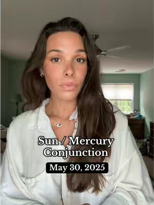A woman with long brown hair is centered in the frame, wearing a white button-down shirt. Text overlays the image, indicating an astrological theme. The background is a softly lit interior with hints of a window and a fan.