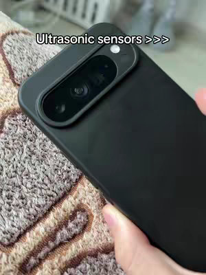 The image shows a close-up view of a black smartphone, held at an angle. The phone has a prominent camera module. The background is a textured, possibly fabric surface, and a hand is visible holding the phone. The focus is on the phone and the text overlay.