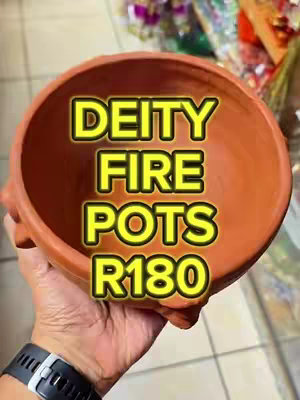 Image shows a hand holding a brown clay bowl against a blurred background. Text overlayed on the bowl reads 'DEITY FIRE POTS R180'. The bowl is round with small handles, and the hand is wearing a watch.
