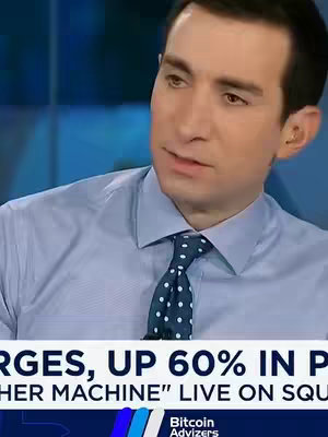 A man in a light blue dress shirt and a dotted tie is speaking in front of a blue background. Text overlays at the bottom of the frame.
