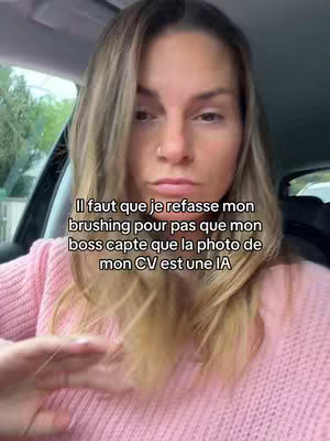 A woman is filmed from the chest up inside a car. She has blonde hair and is wearing a pink sweater. The text overlay says “Il faut que je refasse mon brushing pour pas que mon boss capte que la photo de mon CV est une IA”.