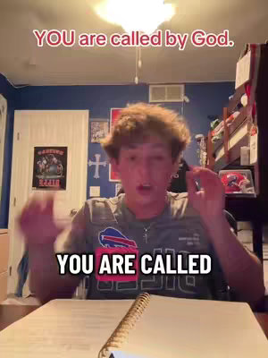 A young man is centered in the frame with a neutral expression, indoors. The background is a mix of various items in a room: a framed picture and a cross. Overlayed text at the top of the frame reads 'YOU are called by God,' in a bold, red font, setting a direct tone. Below and centered, the bold text 'YOU ARE CALLED' appears in white, adding emphasis. The man is wearing a t-shirt. The lighting appears to be from overhead, and the general impression is one of a personal message delivered within what seems to be a bedroom setup.
