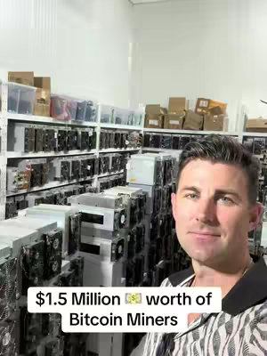 A man stands in a large warehouse filled with rows of computer hardware equipment on shelves. A text overlay at the bottom says '$1.5 Million worth of Bitcoin Miners'.