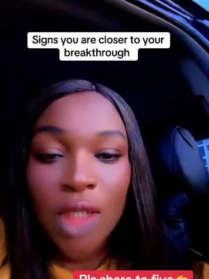 A woman with long dark hair faces the camera, speaking. Above her head is a white banner with black text. The lighting is soft, highlighting her facial features. The background is out of focus, suggesting the image was taken inside a vehicle.
