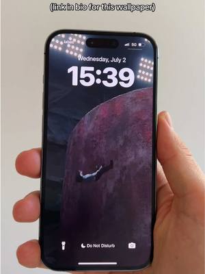 The image shows a smartphone held by a person's hand, displaying a dark background. The screen features a celestial scene depicting a figure falling toward a large, purplish-red planet. The time is shown as 15:39, with Wednesday, July 2 displayed above it. The phone's 'Do Not Disturb' mode is activated.