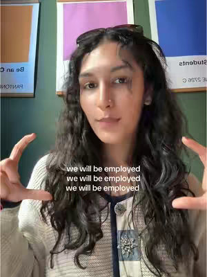 A woman with long curly hair holds her hands up in a gesture, smiling at the camera in a bright setting. Text overlays read, 'we will be employed' repeated three times. The background has colorful art and a green wall.