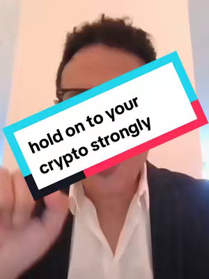 A man with dark hair and glasses is centered in the frame, with a text overlay superimposed on the screen. The text is inside a colored box with a white background and colored borders; it reads, 'hold on to your crypto strongly.' He is likely in an office setting, in front of a white wall and wearing a white collared shirt and a black blazer.