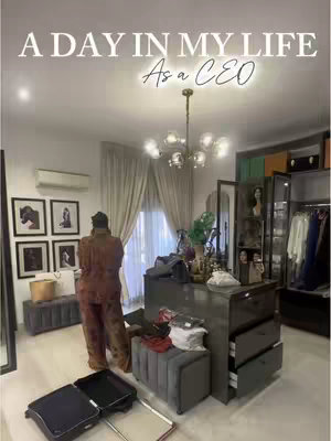 The cover image for the video shows a well-lit walk-in closet. The focus is a person standing with their back to the camera, dressed in coordinated brown patterned clothing, possibly silk pajamas. The closet area contains a large, dark gray dresser, multiple framed artworks, mirrors, and a modern, ornate chandelier. A designer luggage lies on the floor. The overall impression is one of luxury and affluence.