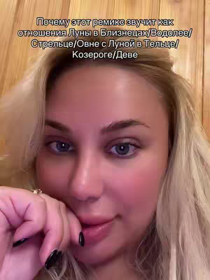 The cover image is a close-up selfie featuring a fair-skinned person with blonde or light-colored hair. The individual has noticeable eye makeup and is looking at the camera with a slightly inquisitive expression. The background features a wooden texture. Overlayed on the image is text in a language, likely discussing something astrology-related.