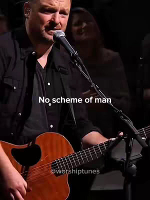Photo of a man singing and playing an acoustic guitar, with text overlaid. The man is in the foreground, with a microphone in front of him. A woman is slightly blurred in the background. The lighting is dim, and the color palette is warm.