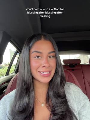 A woman with long black hair is seated inside a car, smiling and looking at the camera. The interior of the car, including the seats and the car's headliner, is visible. A text overlay is present at the top of the image.
