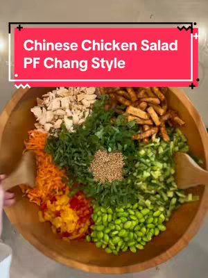 A top-down shot of a wooden bowl filled with a colorful assortment of salad ingredients, including chopped chicken, shredded carrots, various greens, sesame seeds, and edamame.