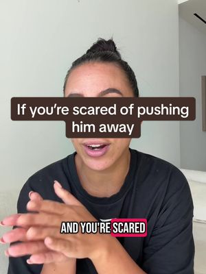 A woman with dark hair pulled back, wearing a black shirt, is centered in the frame, speaking directly towards the camera against a soft background. Over her face is a brown rectangular text overlay with white text, and the bottom displays a pink and white text overlay. The overall composition is bright with neutral tones.