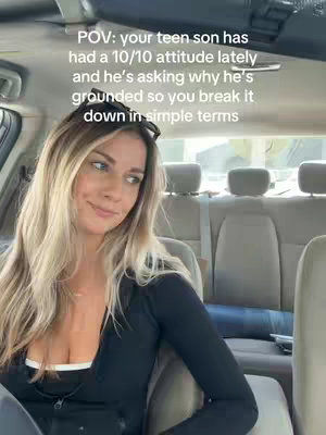 A woman with blonde hair is sitting in the driver's seat of a car, smiling and looking slightly to the side. The caption is superimposed on the video.
