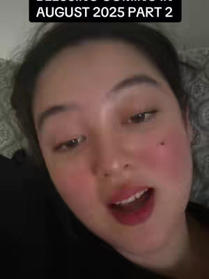 A close-up shot of a woman with pale skin and rosy cheeks, looking slightly off-center. She has dark hair and is wearing a black top. The background is a soft, patterned fabric. Text overlays at the top say AUGUST 2025 PART 2.