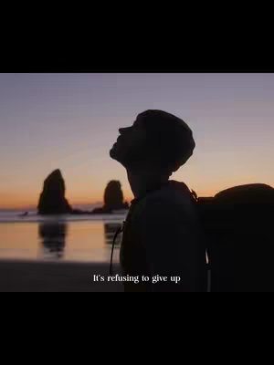 A silhouette of a person standing on a beach, looking upwards towards the sunset. The sky is a gradient of orange and purple, and there are two rock formations in the distance. The text overlay at the bottom reads, 'It's refusing to give up'.