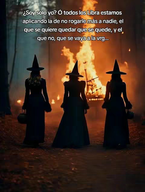 The image shows three women dressed in long black dresses and pointed hats, facing away from the camera, standing in front of a large fire burning in a forest setting.