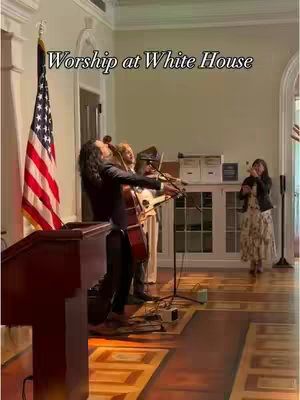 A live performance by a musical group at the White House, with an American flag visible and a woman singing. The image has a warm, inviting tone.